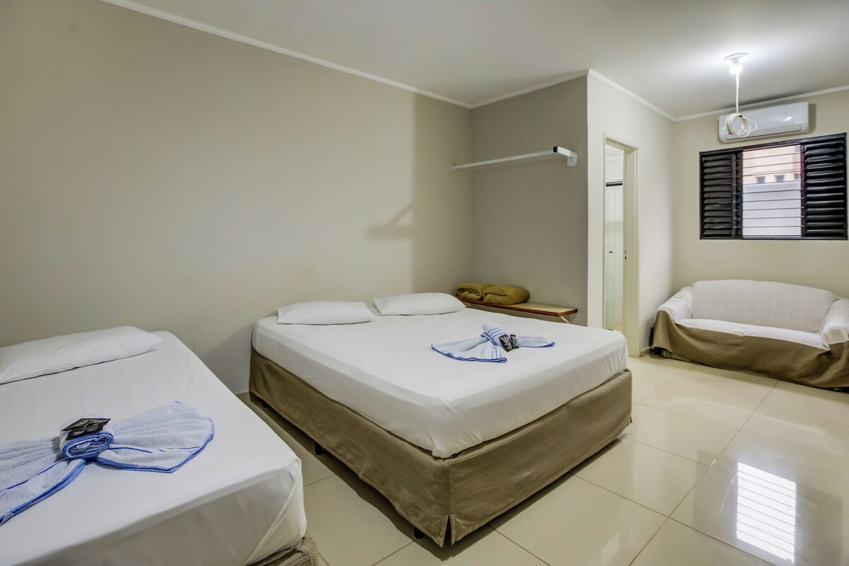 A hotel room with two single beds, a sitting area with a chair, a small table, and an air conditioning unit on the wall.