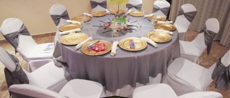 A round table with a grey tablecloth, white chairs with grey sashes, and gold plates.