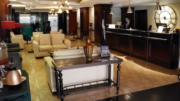 Vestíbulo de hotel con recepción, zona de estar y un gran reloj.