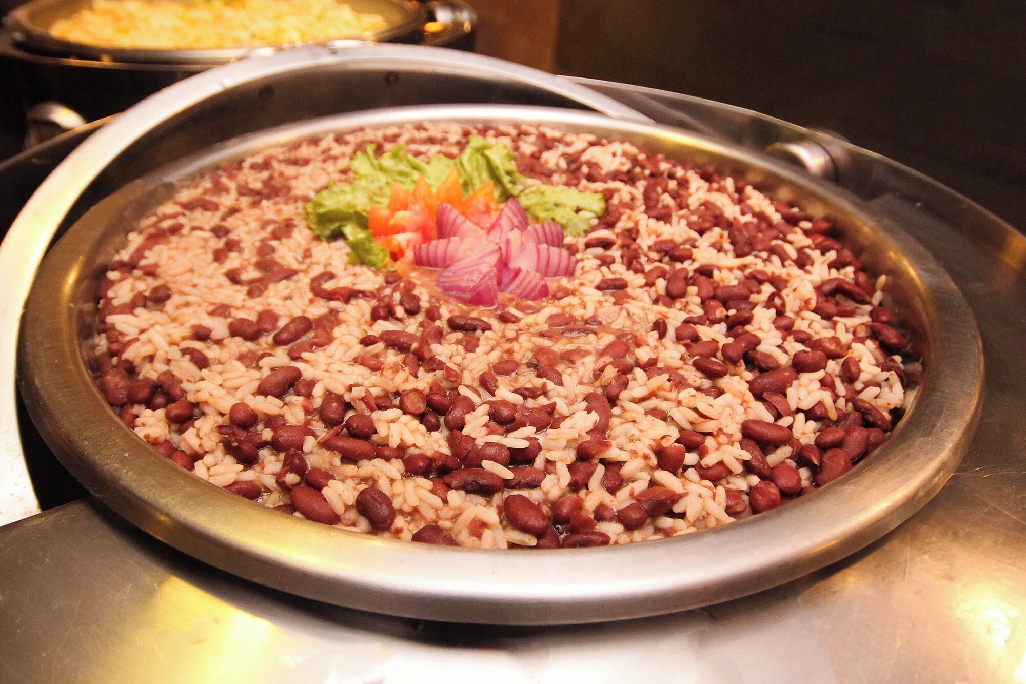 A large metal tray filled with rice and beans, garnished with lettuce and red onion slices.