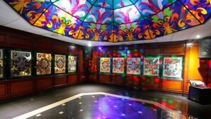 Una habitación con un techo de vitrales coloridos, obras de arte en las paredes y un suelo reflectante.