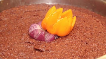 Un tazón de salsa espesa, marrón rojiza, con rodajas de cebolla roja y un pimiento amarillo por encima.