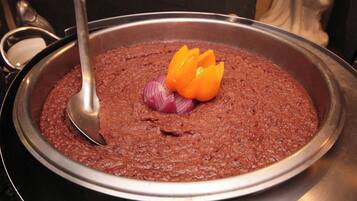 A large metal pan filled with a thick, reddish-brown dish, garnished with sliced red onions and orange bell pepper.