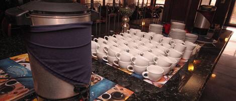 Ein reichhaltiges Buffet mit einer Kaffeemaschine und mehreren weißen Tassen auf einer Theke.