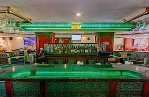 Eine Bar mit einer beleuchteten Theke, Flaschenregalen und einem Fernsehbildschirm.