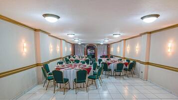 A banquet hall with round tables, green chairs, and white tablecloths.