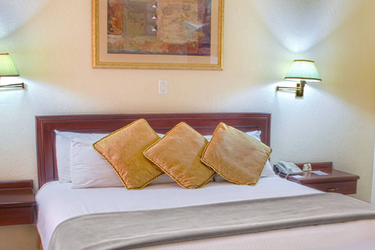 Una habitación de hotel con una cama grande, dos lámparas de noche, una mesita de noche y un cuadro enmarcado en la pared.