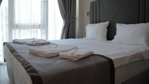 A neatly made bed with pillows and folded towels, a dark headboard, and sheer curtains on a window. - All Inn Hotel (Istanbul)