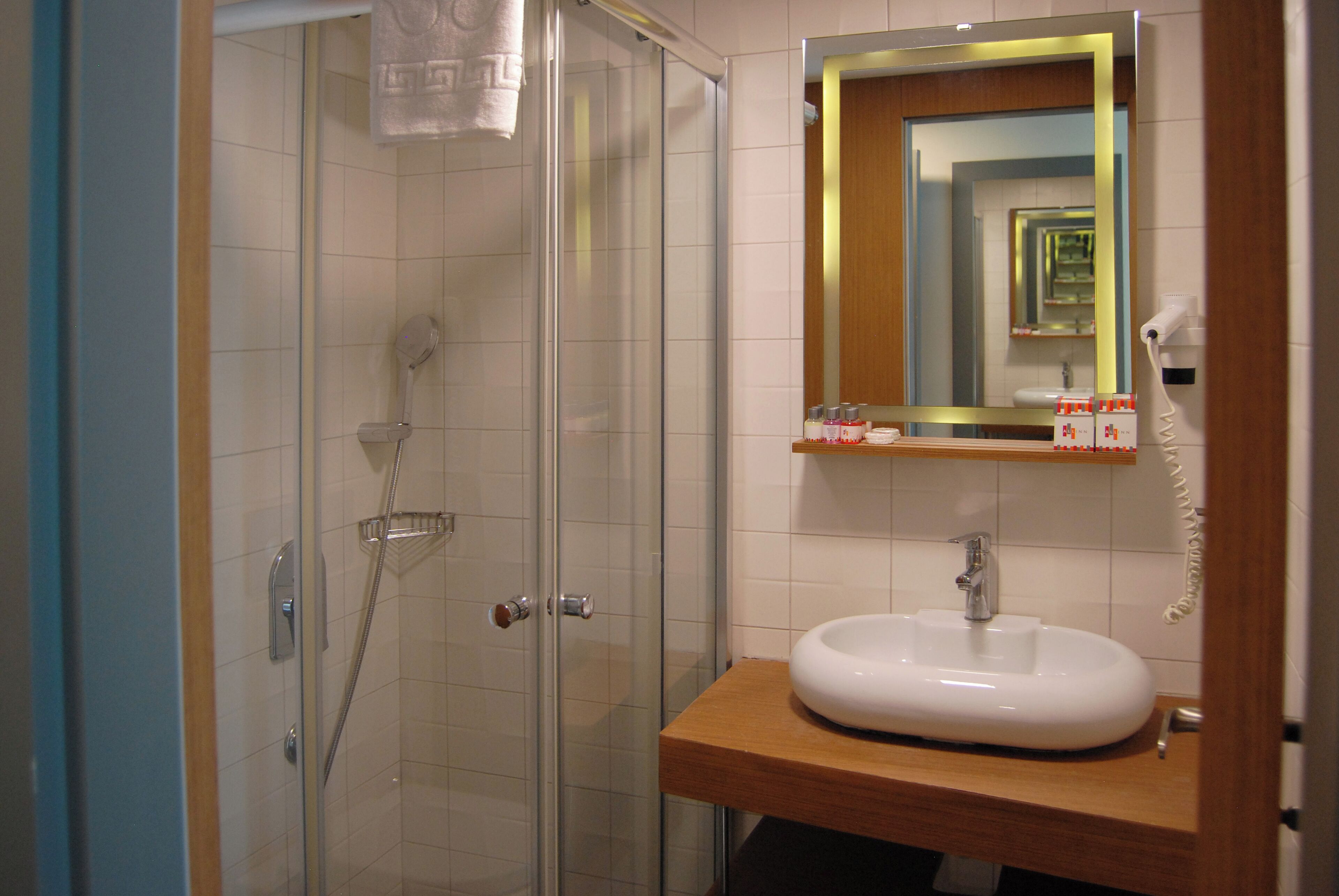 Une salle de bain dotée d’une douche à parois de verre, d’un lavabo blanc avec un plan de toilette en bois et d’un miroir avec un cadre doré.