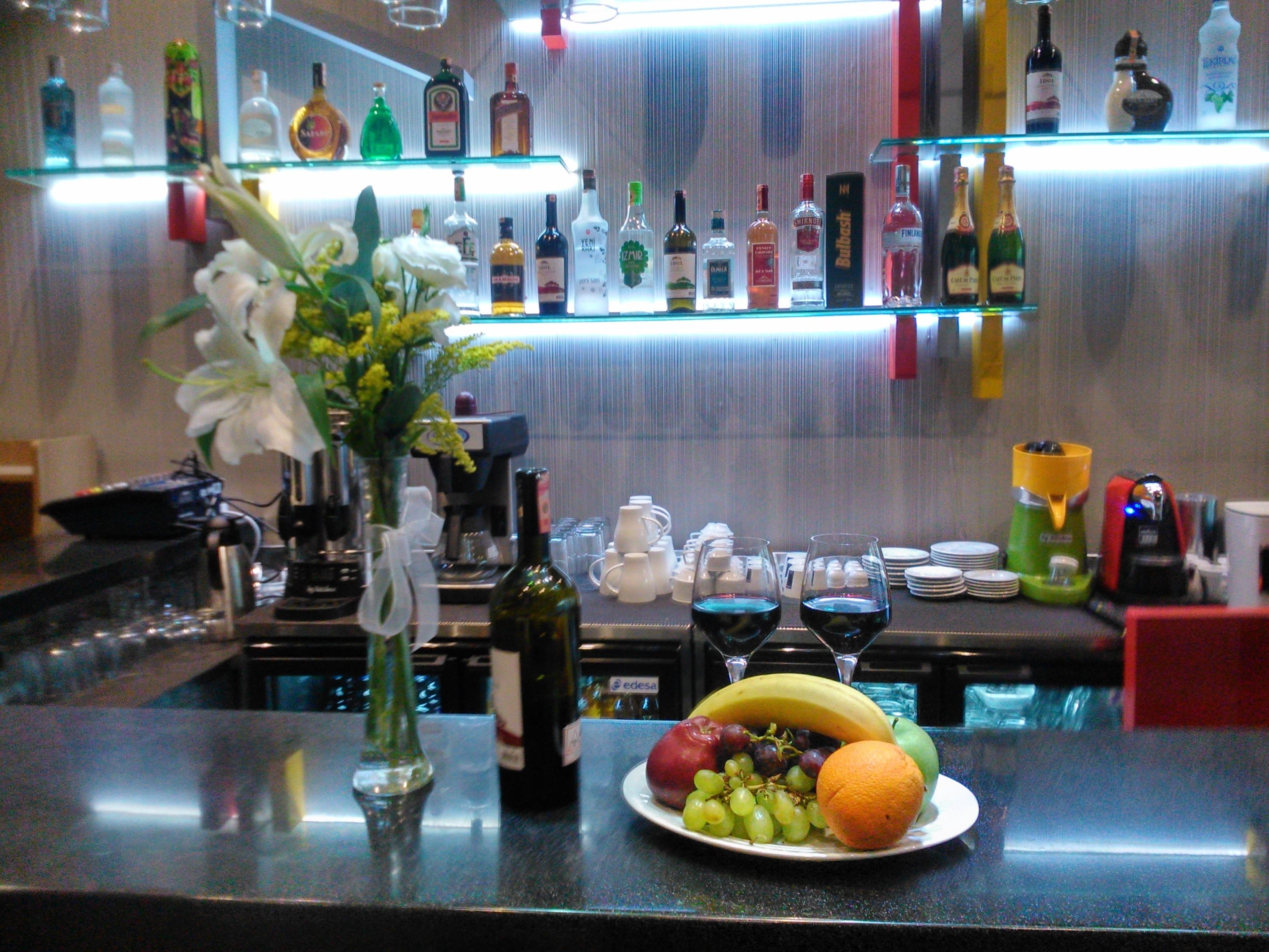 Una zona de bar con varias botellas de licor, una máquina de café y un plato de fruta sobre el mostrador.
