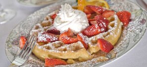 A plate of waffles topped with whipped cream and strawberries, dusted with powdered sugar.