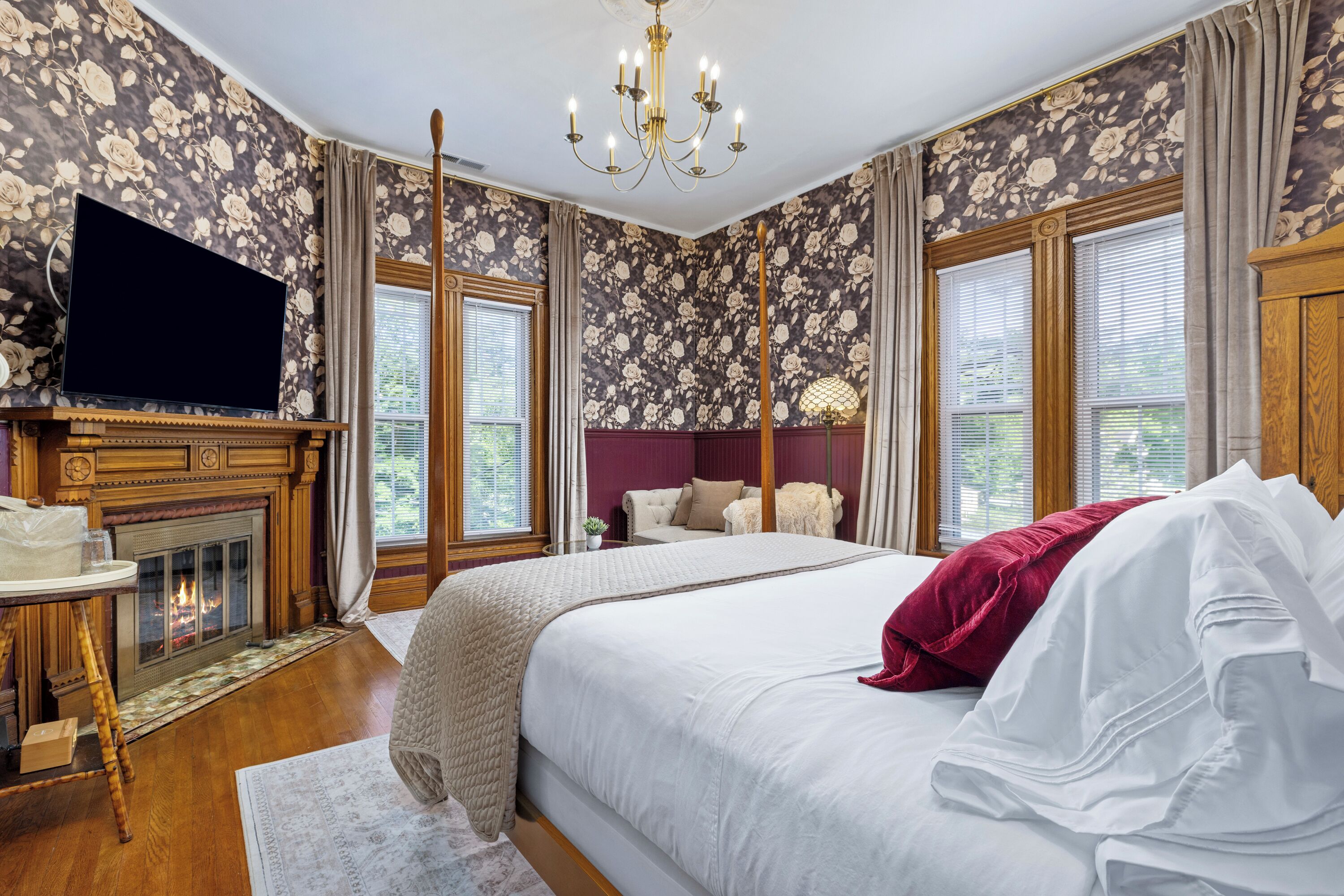 A bedroom with a large bed, a television, a fireplace, and floral wallpaper.