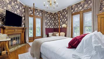 A bedroom with a large bed, a television, a fireplace, and floral wallpaper.