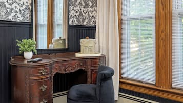 A room with a dark wooden desk, a chair, a potted plant, and a window with blinds.