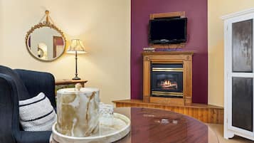 A living room with a fireplace, a television mounted above it, a round wooden coffee table, and a blue armchair with a decorative pillow.