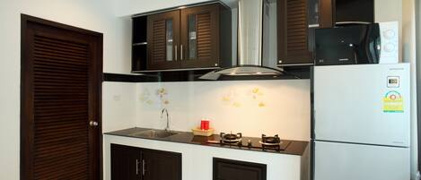 A compact kitchen with dark cabinetry, a stainless steel range hood, a built-in microwave, and a refrigerator.