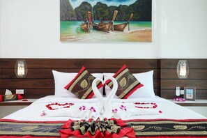 Una cama bien hecha con una toalla dispuesta en forma de corazón, un cojín decorativo y una colcha estampada con motivos florales.