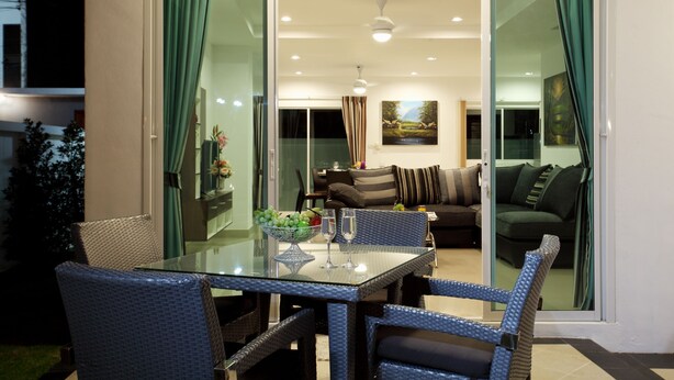 Een moderne woonkamer met een glazen deur die uitkomt op een balkon, ingericht met rieten stoelen en een glazen tafel.