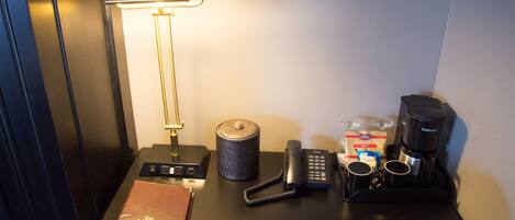 A hotel room desk with a lamp, a phone, a coffee maker, a tissue box, and a book.