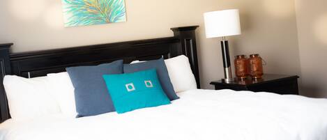 A neatly made bed with white and teal pillows, a headboard, and a wall-mounted artwork.