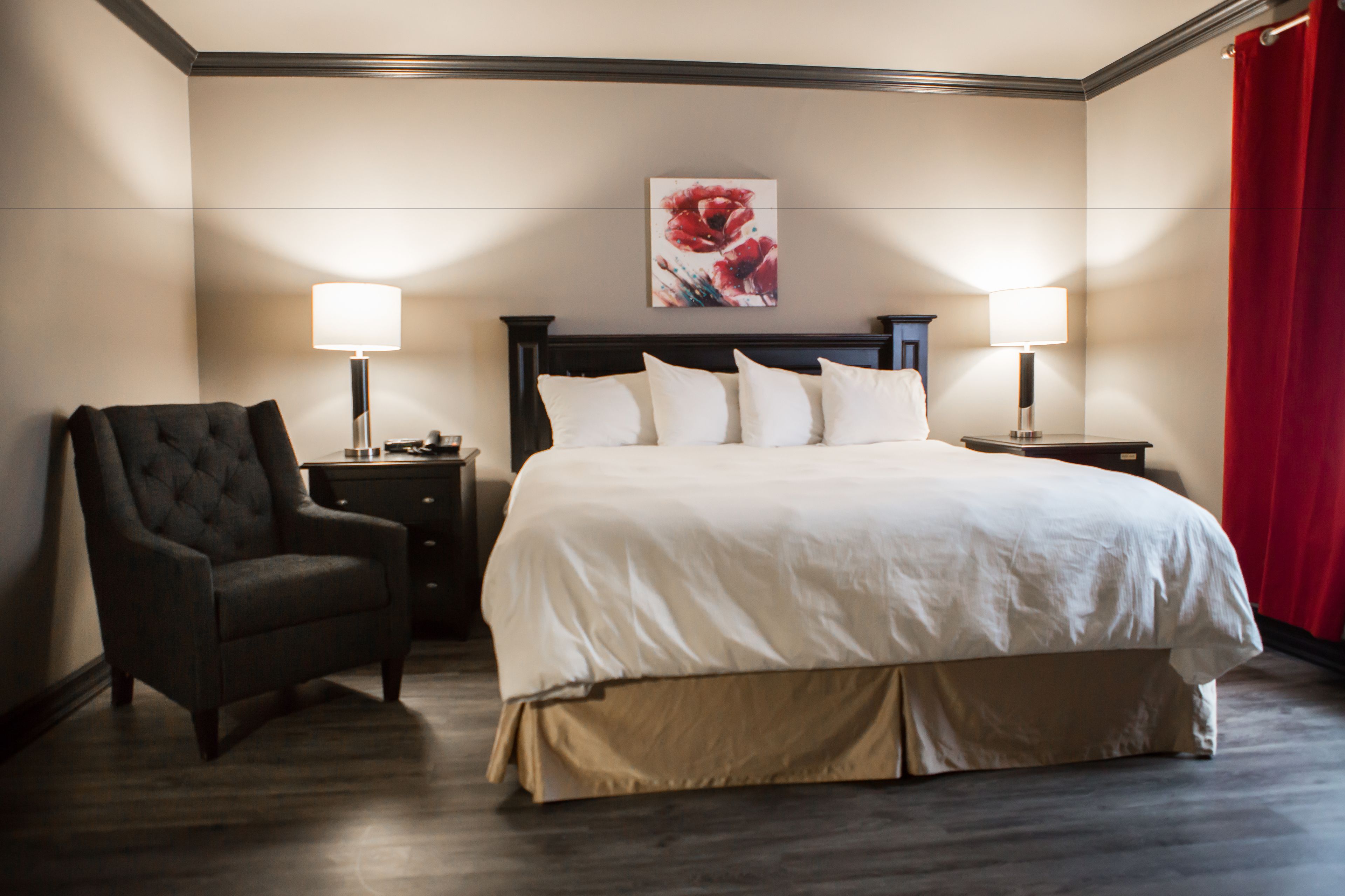 A hotel room with a large bed, two bedside tables with lamps, a dark armchair, and a floral artwork on the wall.