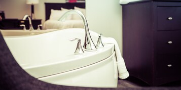 A modern bathroom with a white bathtub, a single faucet, and a dark wooden cabinet.