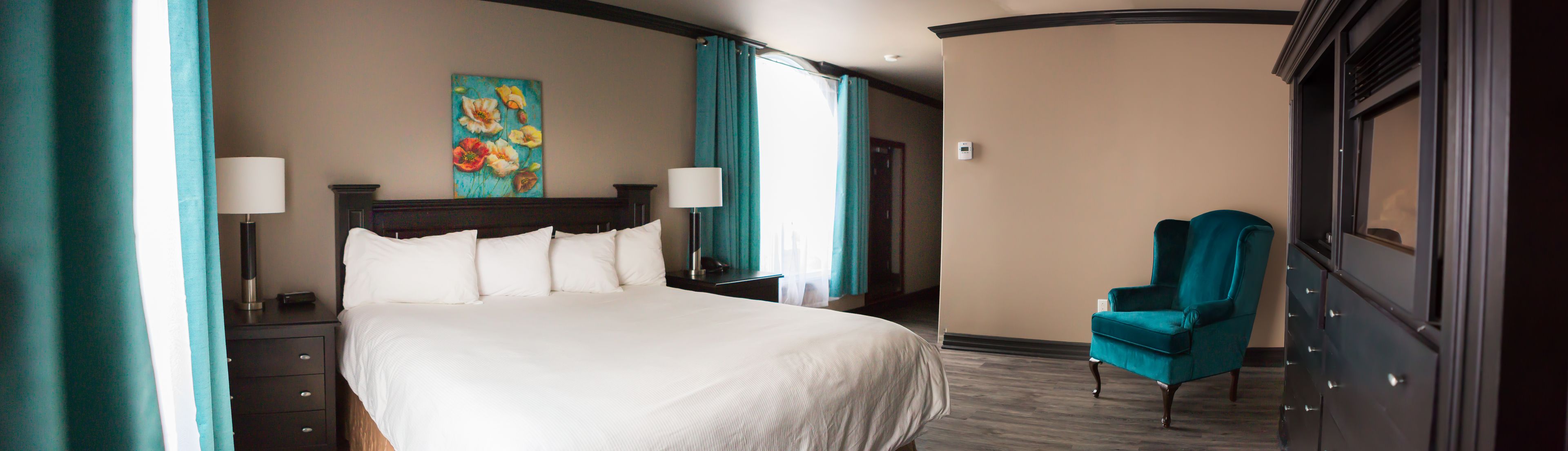 A hotel room with a large bed, two bedside tables, a chair, a painting on the wall, and a window with curtains.