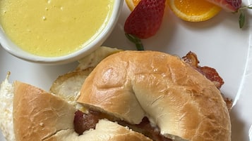 A plate with a sandwich cut in half, a bowl of soup, and sliced strawberries and oranges.