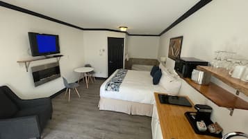 Quarto de hotel com cama, escrivaninha com lavatório, televisão, mesa pequena e cadeira.