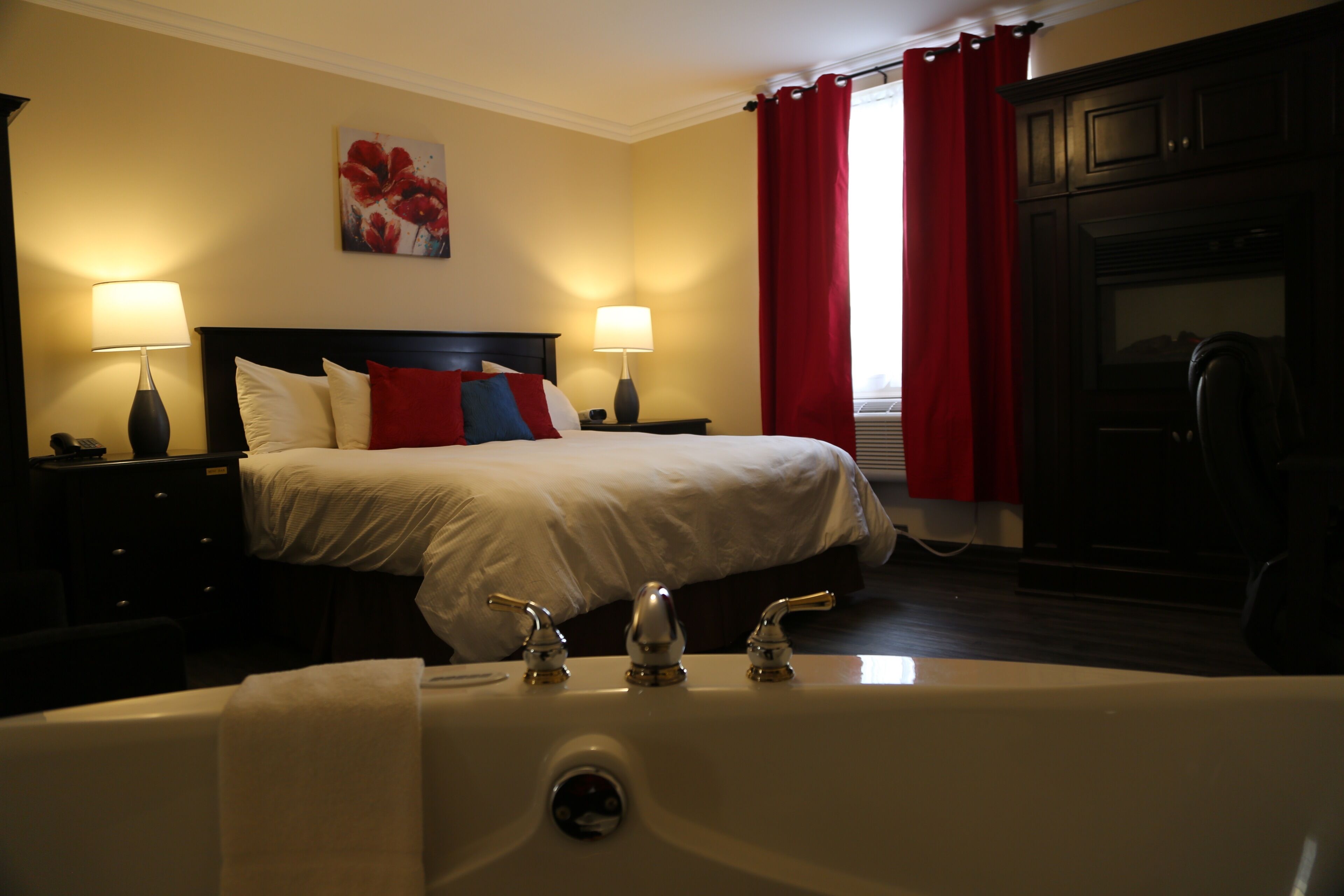 Una camera d'albergo con un letto grande, due lampade sui comodini, una tenda rossa e una vasca da bagno.