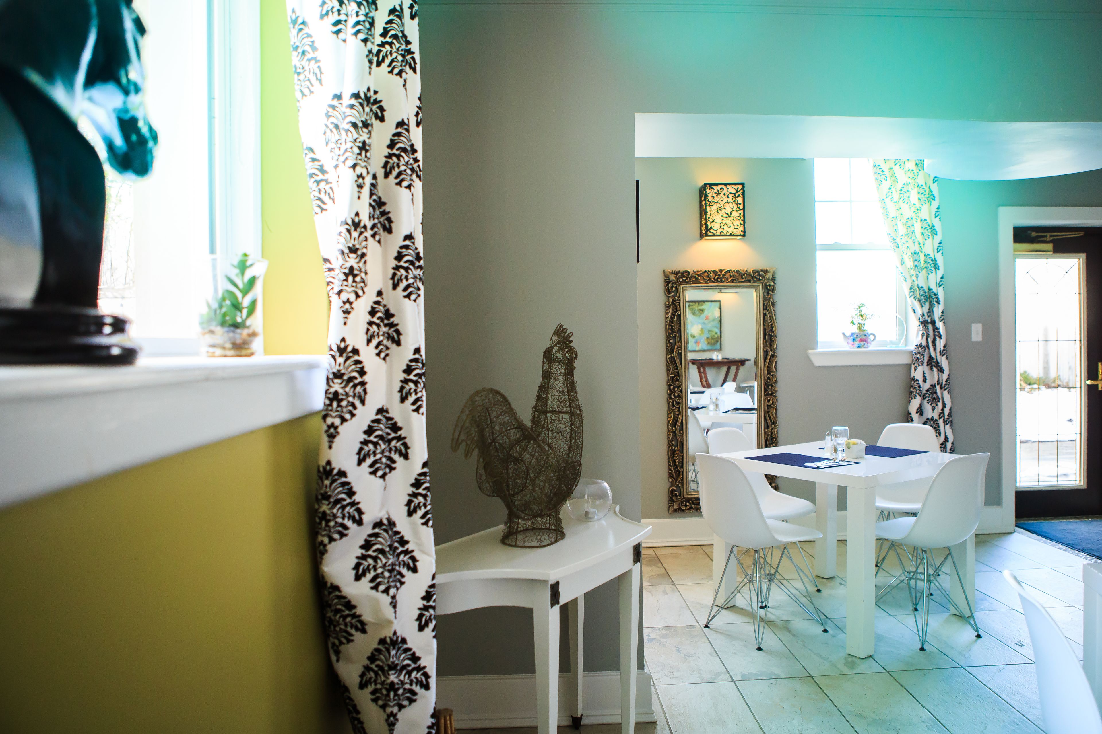 A dining area with a white table and chairs, a decorative rooster sculpture, and a mirror on the wall.