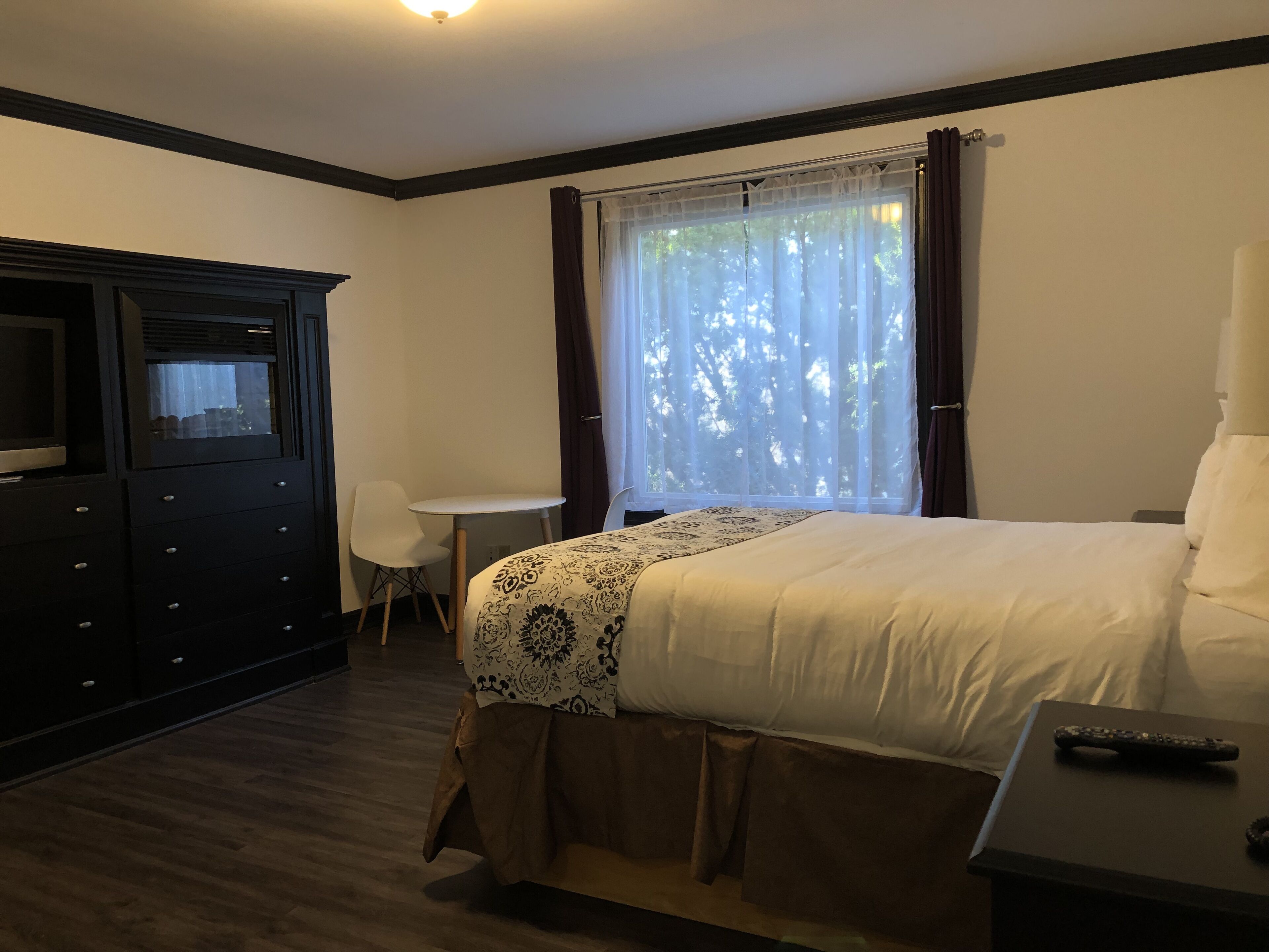 A hotel room with a bed, a desk, a chair, a TV, and a window with curtains.