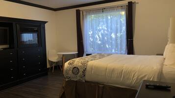 A hotel room with a bed, a desk, a chair, a TV, and a window with curtains.