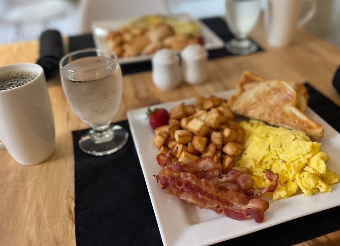 A breakfast plate with scrambled eggs, bacon, toast, and hash browns.