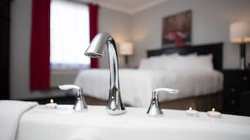 Un baño de hotel con un lavamanos moderno, dos grifos y dos velas encendidas sobre el mostrador.