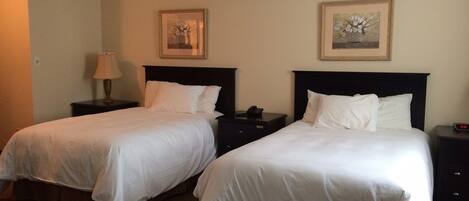 Two single beds with white linens, nightstands with lamps, and framed floral artwork on the walls.