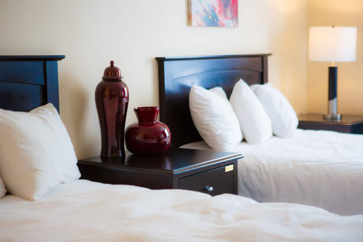 Et hotelværelse med to senge, et natbord med en vase, en lampe og et billede på væggen.