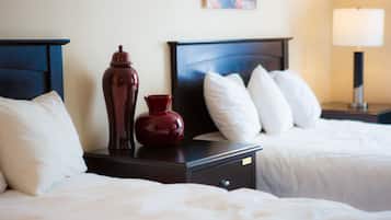 Een hotelkamer met twee bedden, een nachtkastje met een vaas, een lamp en een schilderij aan de muur.