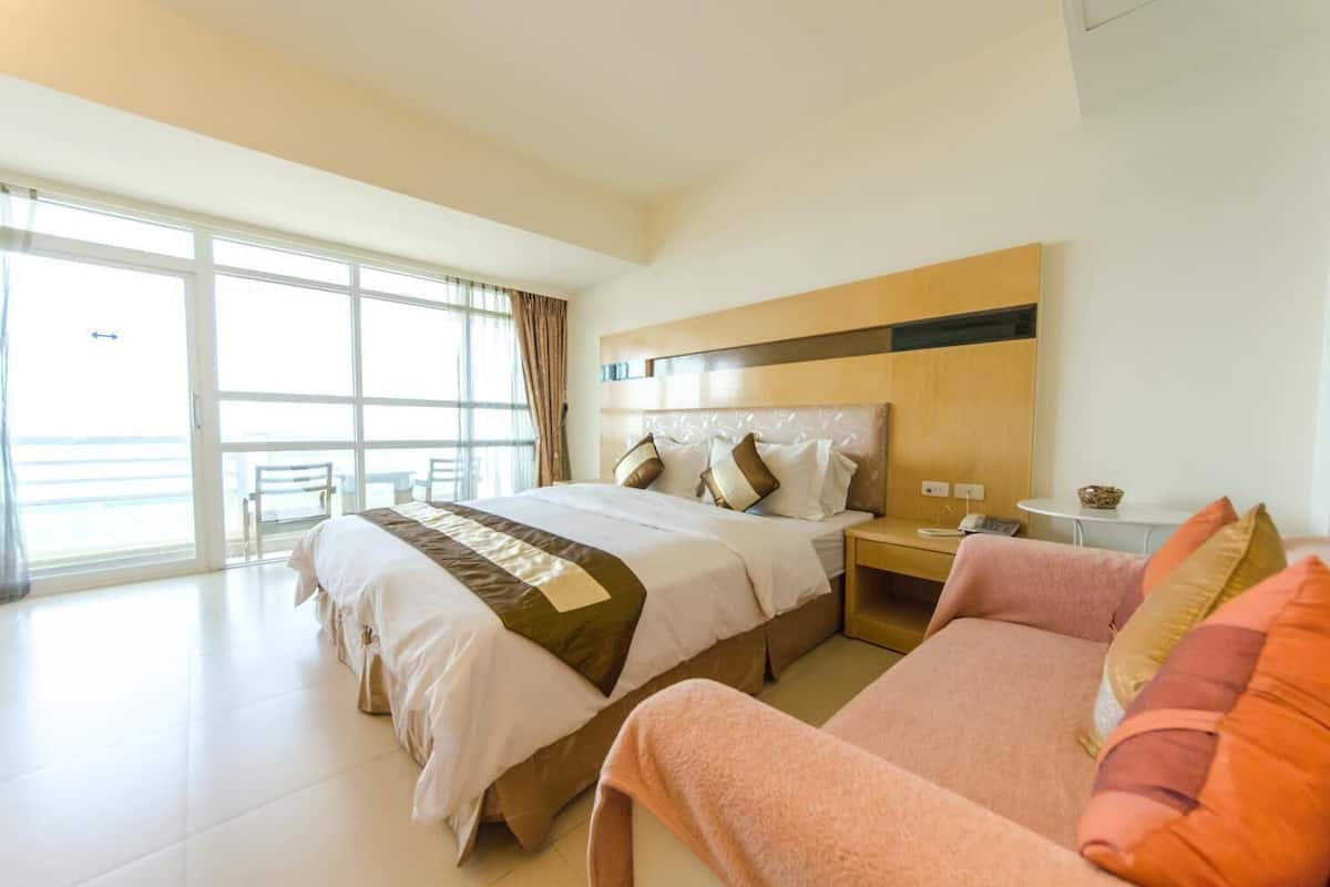 A hotel room with a large bed, a desk, a chair, and a sofa.