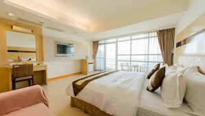 Une chambre d’hôtel avec un grand lit, un bureau avec une chaise, une télévision et un balcon équipé d’une table et de chaises.