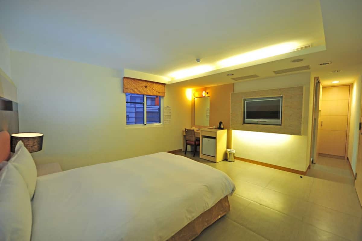 A hotel room with a bed, desk, chair, and a TV mounted on the wall.
