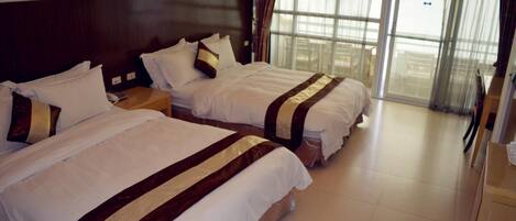 Habitación de hotel con dos camas, cabecera de madera, un ventanal grande con cortinas y un escritorio de madera.