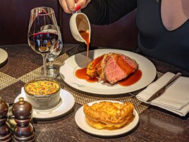 Una mesa de comedor con un plato de comida, una copa de vino tinto y un bol de sopa.