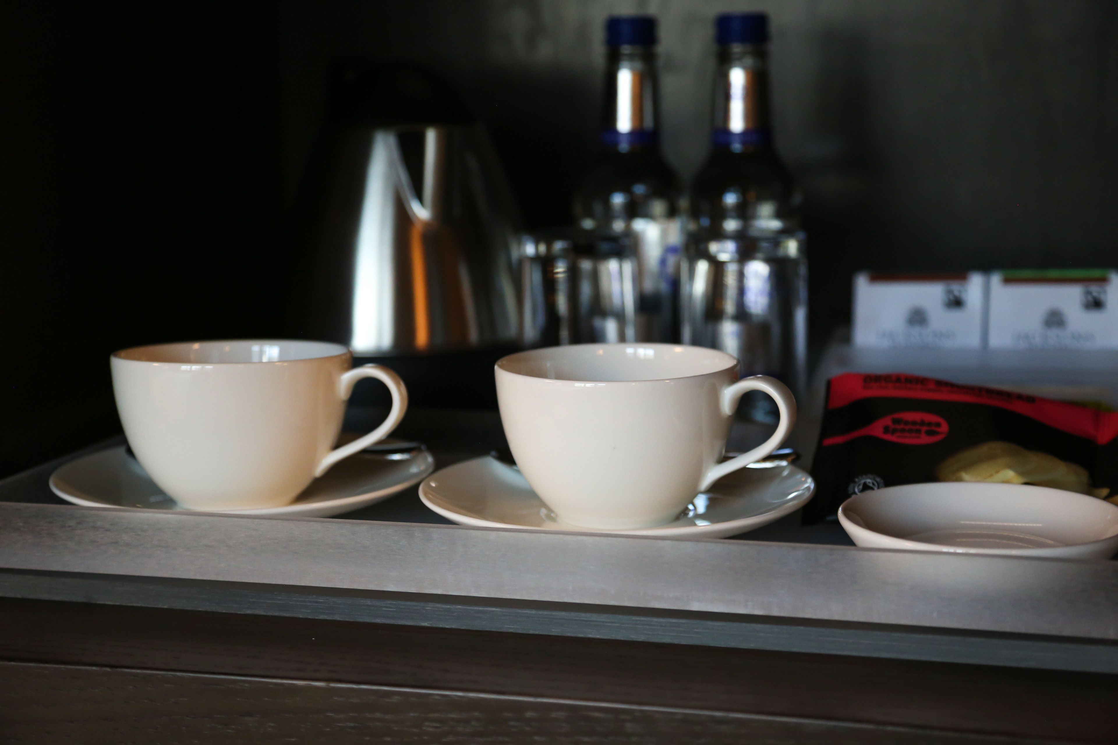 Una bandeja con dos tazas y platillos blancos, un cuenco pequeño y una caja de café orgánico.