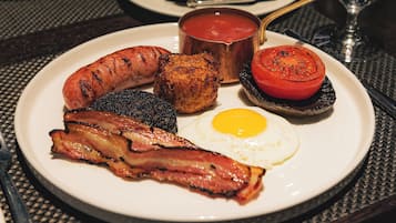 A breakfast plate with bacon, sausages, eggs, and tomatoes.