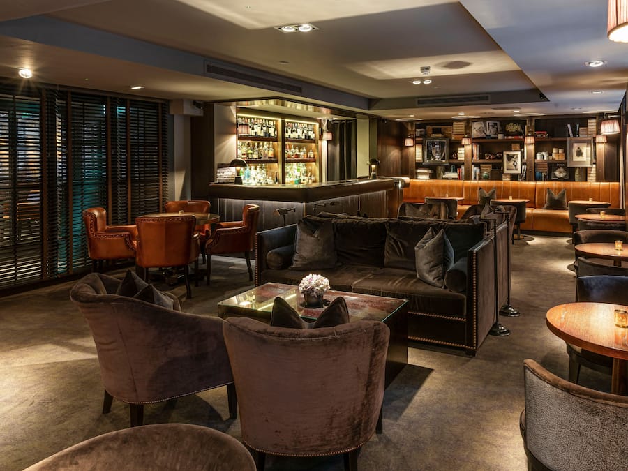 A bar area with a bar counter, seating, and a bookshelf with various items.