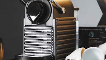 Una máquina de café Nespresso con diseño negro y cromado, sobre una encimera negra con una lámpara al fondo.