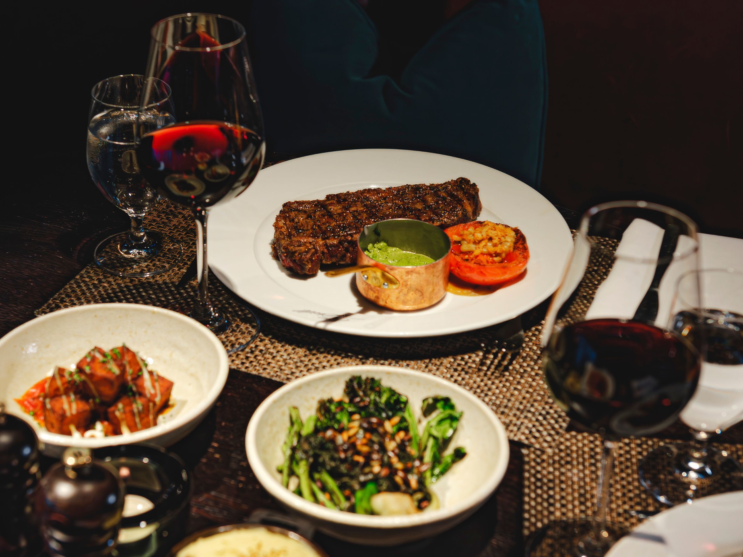 A dining table with a variety of dishes, including a steak, vegetables, and a bowl of soup. There are also wine glasses and a napkin on the table.