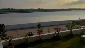 A view of a river with a distant shoreline, a grassy area with potted plants, and a clear sky. - Rainbowsea B&B (Huxi)