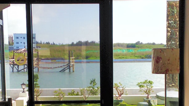 A modern living room with a large sliding glass door leading to a private outdoor area with a lawn and a view of a body of water. - Rainbowsea B&B (Huxi)